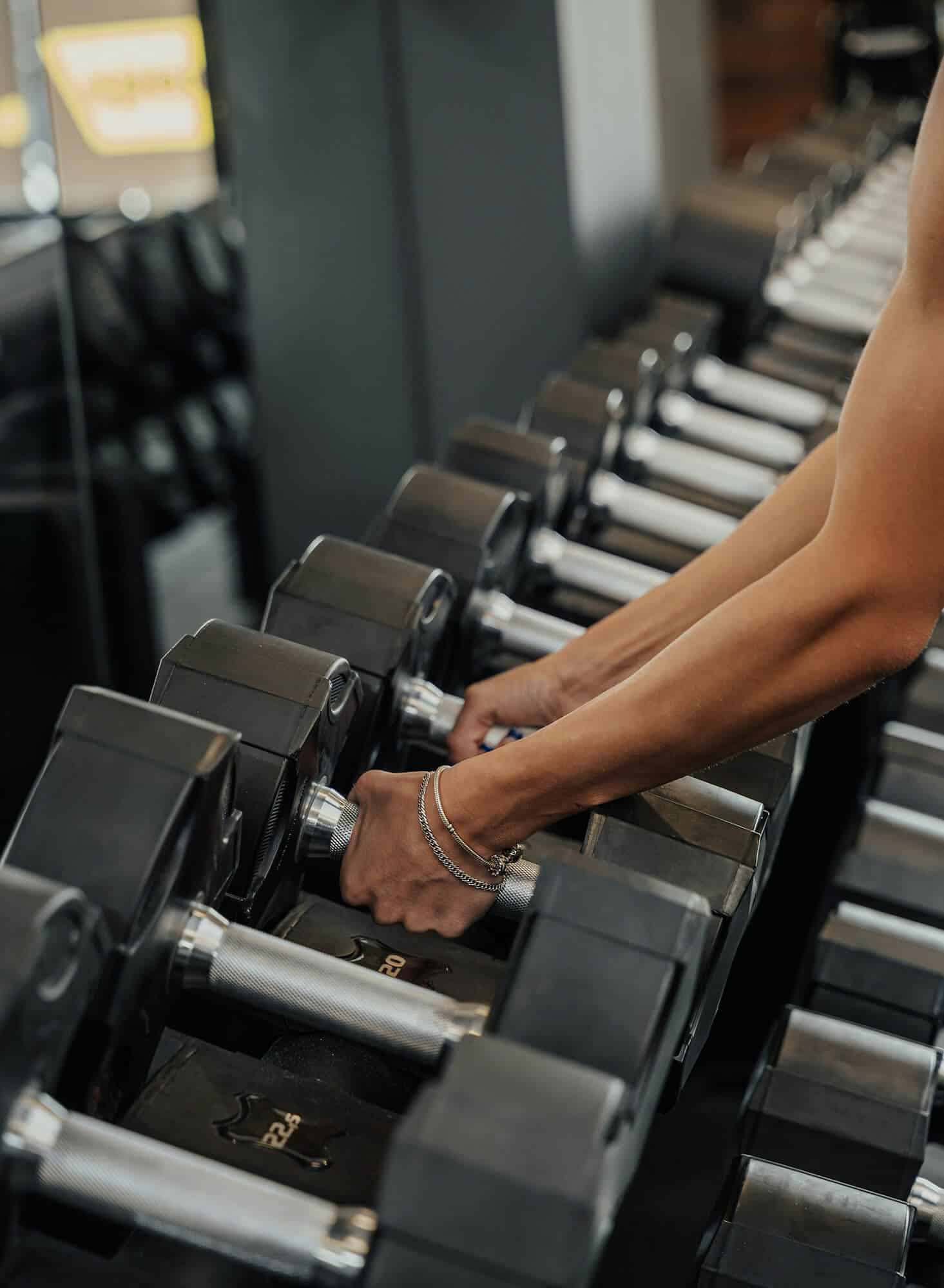 Person grabbing two dumbbells from a row of dumbbells depicting the active lifestyle at Flora apartments in summerville sc - roberto shumski o EjUZo8AKk unsplash